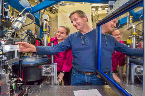 A man dressed in blue showing lab equipment with a woman in red looking over his shoulder.