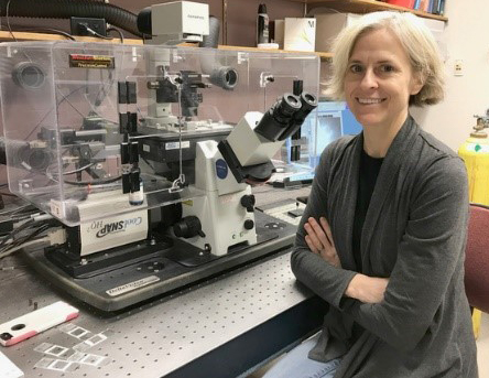 Jennifer “Jake” DeLuca sitting in front of a microscope in a lab.