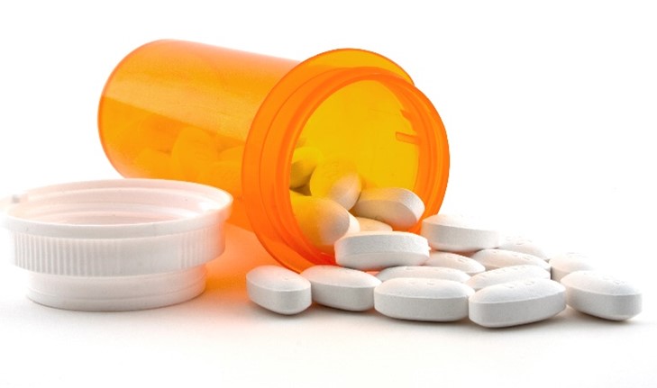 An orange pill bottle lying open on its side with white tablets spilling out of it.