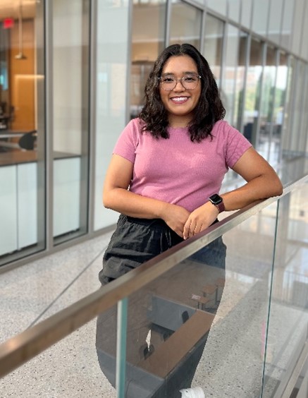 A portrait image of Karen Juanez in a long hallway of a building, leaning against a metal railing.