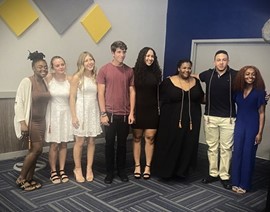 A group of eight people posing for a picture with graduation cords draped around their necks.