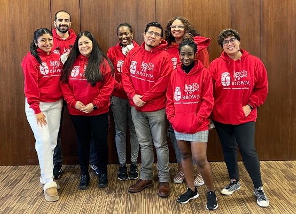 A group of eight people wearing matching red Brown University sweatshirts, posing for a picture. 