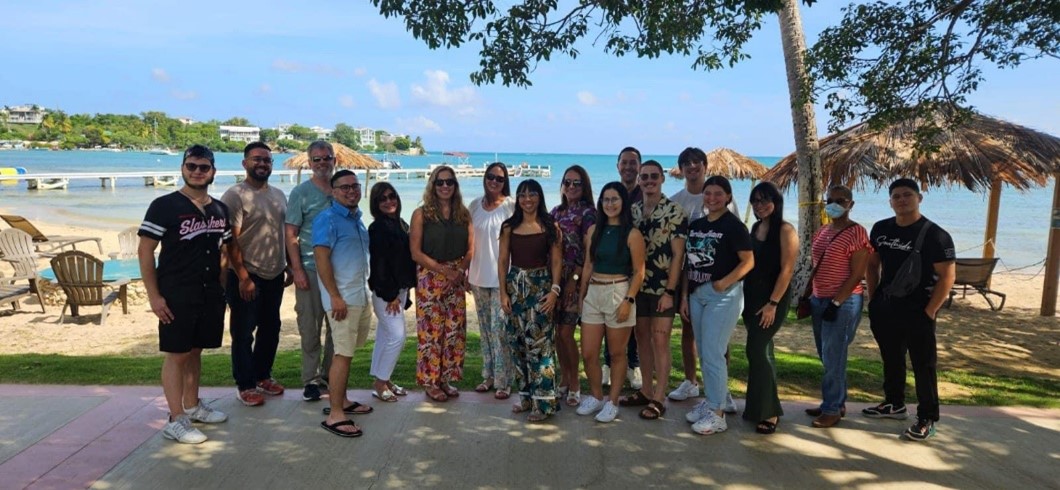 Dr. Appleyard standing outside with 16 other people in a line with the ocean in the background.