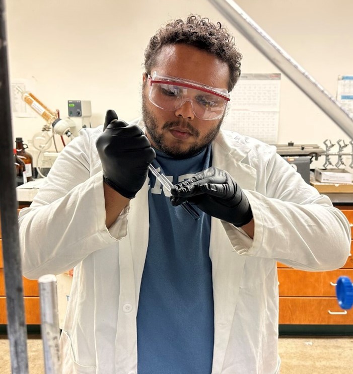 Dr. Glenn Gilyot wearing safety glasses and gloves while pipetting a liquid from a tube. 